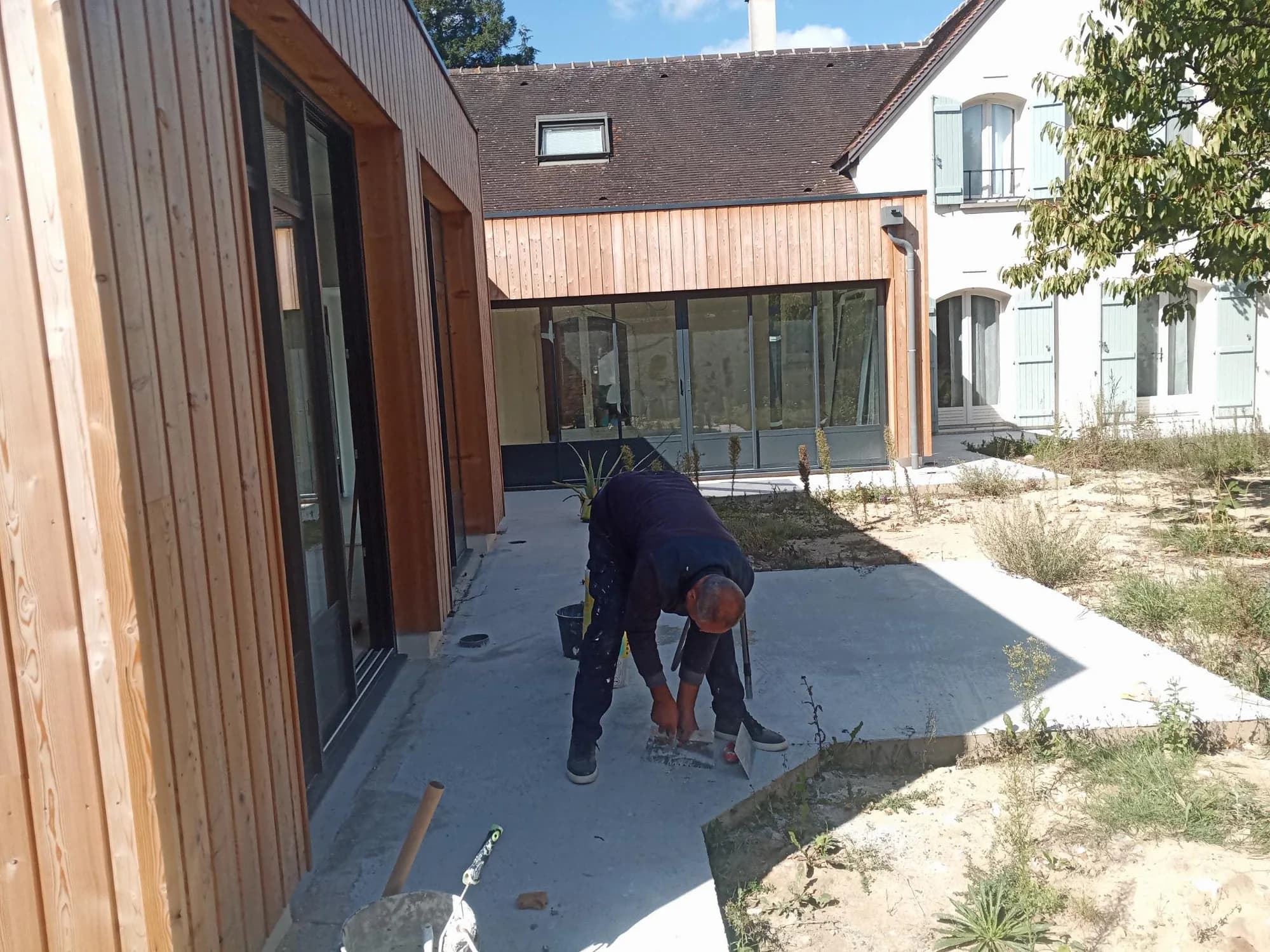 Extension en bardage bois donnant sur une cour intérieure, artisan au travail sur la terrasse