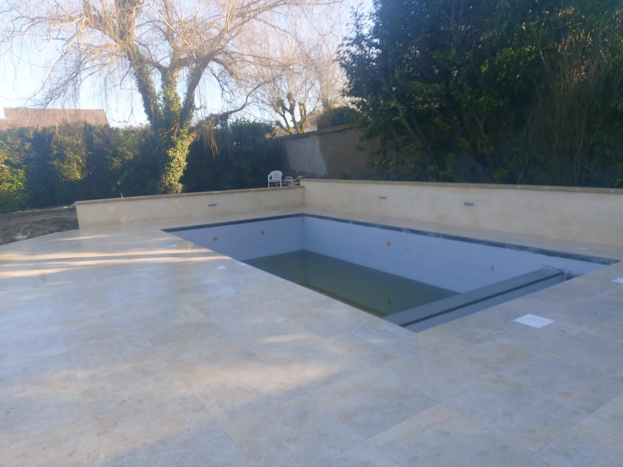 Piscine terminée avec sa plage en pierre reconstituée dans un jardin clos